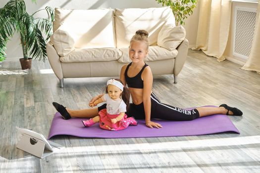 Little cute girl is practicing gymnastics at home. Video lesson. Kid repeating exercises while watching online yoga gymnastics session. Beautiful girl doing fitness exercise at home