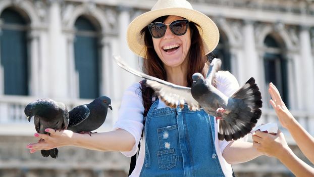 VENICE, ITALY - JULY 7, 2018: portrait of happy woman, tourist, holding pigeons, feeding, play with them, having fun on Piazza San Marco, St Mark's Basilica, on a summer day. High quality photo