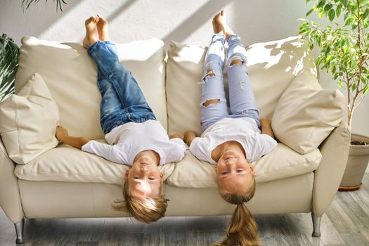 Pretty little girl and boy are lying on their backs on sofa in living room, looking at camera and smiling while playing at home