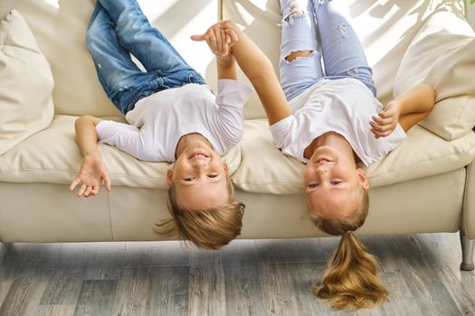 Pretty little girl and boy are lying on their backs on sofa in living room, looking at camera and smiling while playing at home