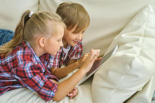 family, children, technology and home concept - smiling brother and sister with tablet pc computer on the sofa in living room