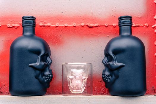 glass gin bottles in the shape of a human skull and a glass stack in the shape of a skull. Drink for a night party on a gray metal background