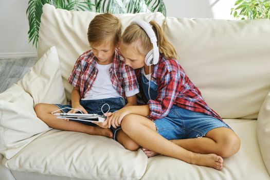 Cute brother and sister with headphones enjoying tablet at home. family, children, technology and home concept