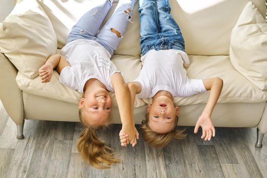 Pretty little girl and boy are lying on their backs on sofa in living room, looking at camera and smiling while playing at home