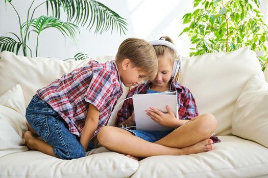 Cute brother and sister with headphones enjoying tablet at home. family, children, technology and home concept