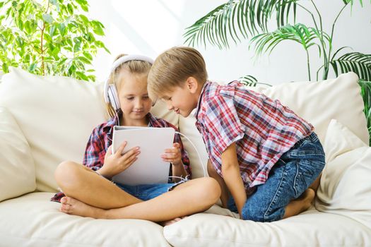 Cute brother and sister with headphones enjoying tablet at home. family, children, technology and home concept