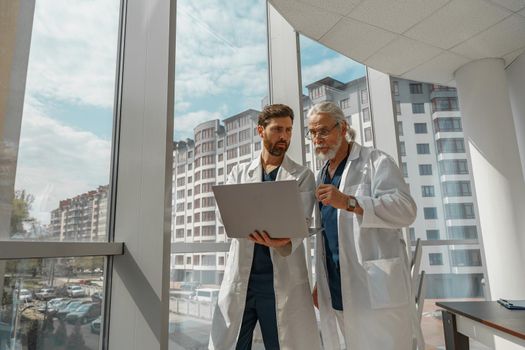 Two doctor colleagues discussing patient diagnosis stand in medicine clinic near panoramic windows