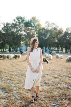 Girl in a straw hat stands on the lawn with grazing sheep. High quality photo