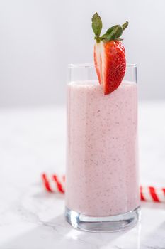 Freshly made healthy breakfast strawberry banana smoothie garnished with fresh strawberry and paper straw.