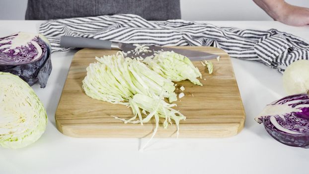 Step by step. Shredding organic cabbage on a wood cutting board.