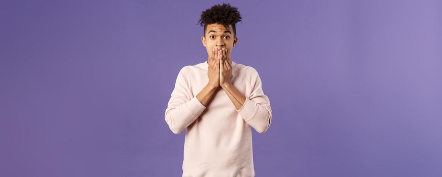 Portrait of shocked, impressed young hispanic hipster guy being astounded by recent news on TV, hold hands on mouth, raise eyebrows cant believe its really happening, stand startled.