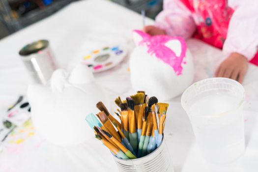 Little girl painting Halloween pumpkin with acrylic paint.