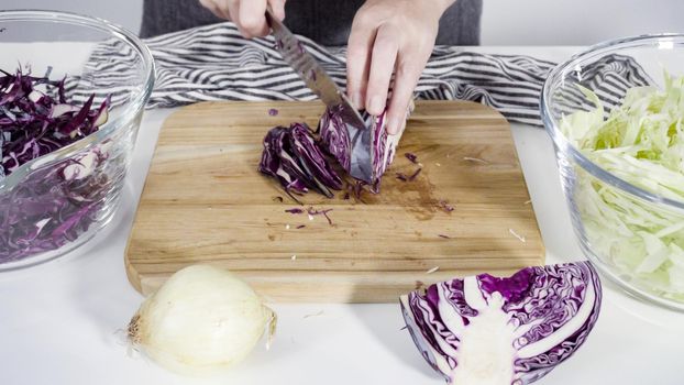 Step by step. Shredding organic cabbage on a wood cutting board.