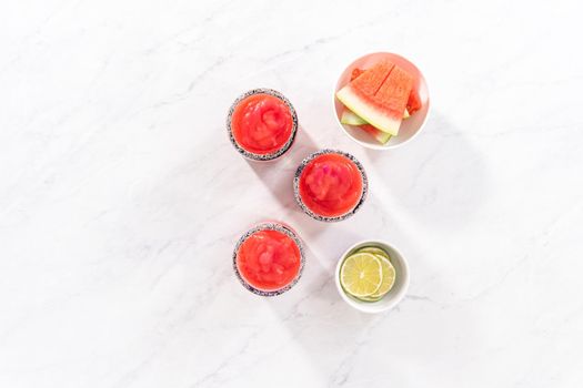 Flat lay. Frozen watermelon margarita in a glass garnished with salt, a slice of fresh watermelon, and lime.