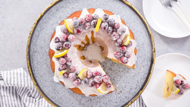 Flat lay. Step by step. Slicing lemon cranberry bundt cake decorated with sugar cranberries and lemon wedges.