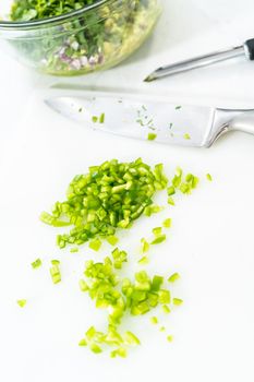 Cutting ingredients on a white cutting board to make classic guacamole dip.