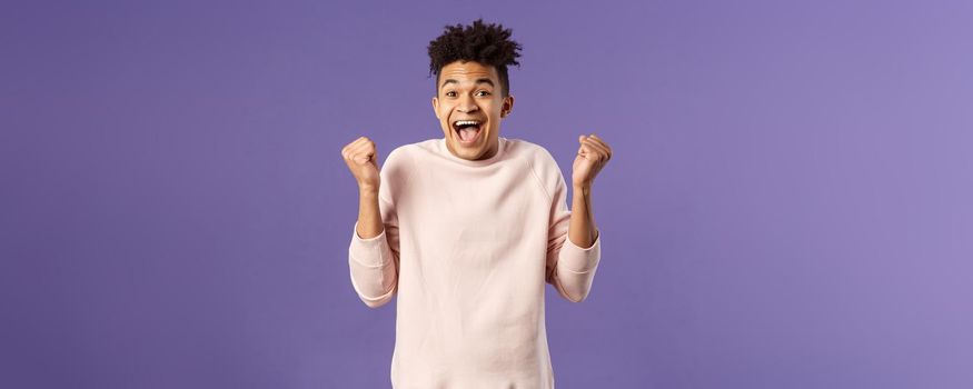 Portrait of happy, cheerful triumphing young hipster guy with dreads, dancing like champion, celebrating success or victory, passed test, fist pump smiling and rejoicing, purple background.