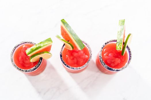 Frozen watermelon margarita in a glass garnished with salt, a slice of fresh watermelon, and lime.