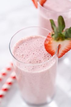 Freshly made healthy breakfast strawberry banana smoothie garnished with fresh strawberry and paper straw.