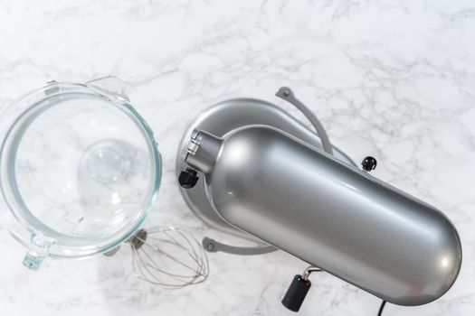 Mixing ingredients in a large glass mixing bowl of kitchen mixer to make eggnog buttercream frosting.