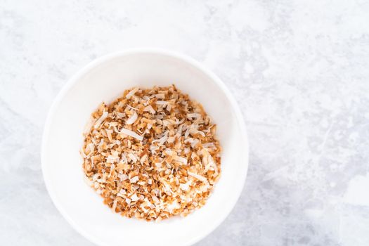 Toasted shredded coconut flakes in a white ceramic bowl.