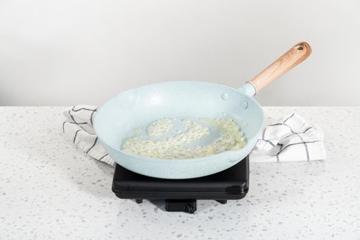 Frying onion and red bell pepper in olive oil on a nonstick frying pan to bake turkey empanadas.