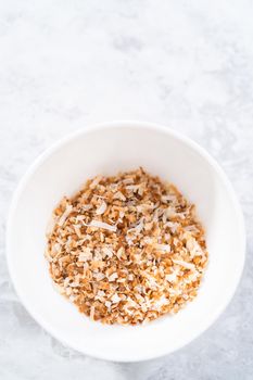 Toasted shredded coconut flakes in a white ceramic bowl.