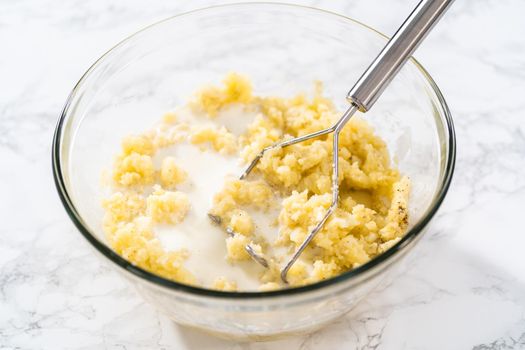 Mashed potatoes. Mashing cooked potatoes in a glass mixing bowl with a potato masher to make mashed potatoes.