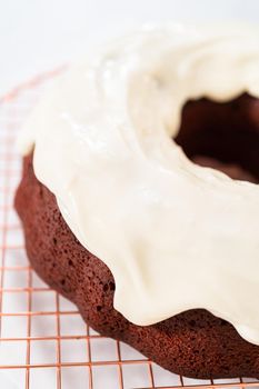 Pouring cream cheese glaze over freshly baked red velvet bundt cake.