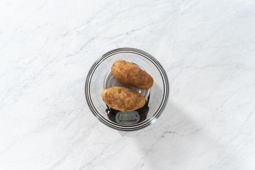 Flat lay. Pressure Cooker Baked Potatoes. Measuring raw potatoes in a glass mixing bowl on the kitchen scale.