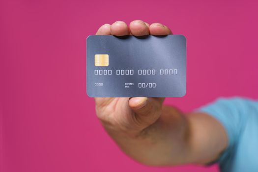 Dark grey-purple debit, credit card in man hand isolated on pink background. Financial, banking concept. No face visible.