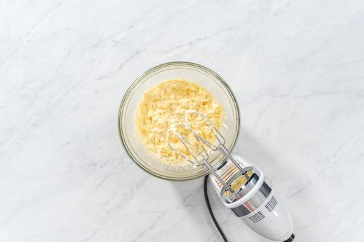 Flat lay. Mixing ingredients in a large glass mixing bowl to make the cream cheese filling for bundt cake.