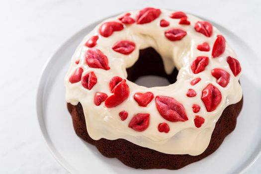 Freshly baked red velvet bundt cake with chocolate lips and hearts over cream cheese glaze for Valentine's Day.