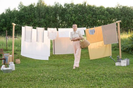 Laundry day. A woman hangs linen and towels on a tree in the courtyard of a village house. Summer cottage concept.