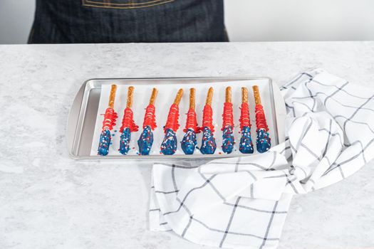 Homemade chocolate-covered pretzel rods decorated like the American flag drying on a baking sheet lined with parchment paper.