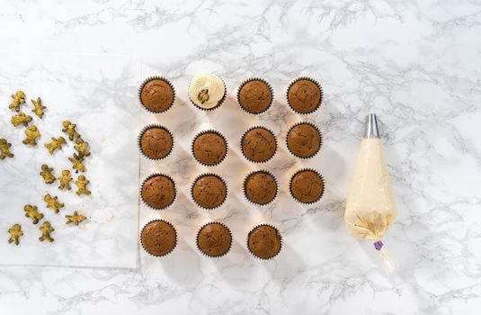 Piping eggnog buttercream frosting on top of gingerbread cupcakes and topping with a chocolate gingerbread man.