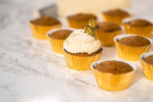 Piping eggnog buttercream frosting on top of gingerbread cupcakes and topping with a chocolate gingerbread man.