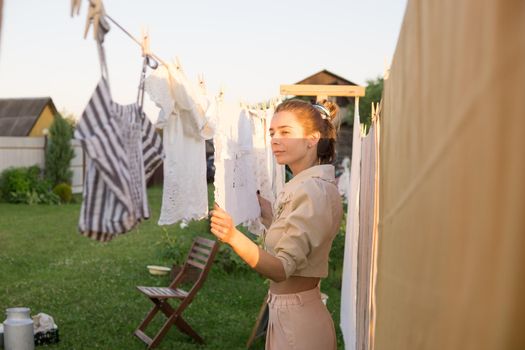 Laundry day. A woman hangs linen and towels on a tree in the courtyard of a village house. Summer cottage concept.