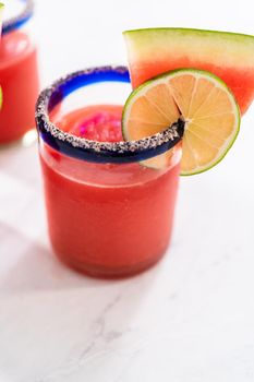Frozen watermelon margarita in a glass garnished with salt, a slice of fresh watermelon, and lime.