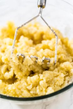 Mashed potatoes. Mashing cooked potatoes in a glass mixing bowl with a potato masher to make mashed potatoes.