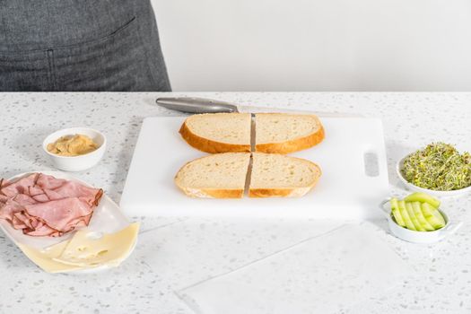 Assembling ham, cucumber, and sprout sandwiches on the white cutting board.