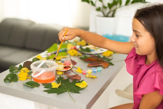 A child paints a picture of an autumn leaf with paints. Children's hands. Favorite hobby, materials for creativity. High quality photo