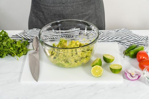Cutting ingredients on a white cutting board to make classic guacamole dip.