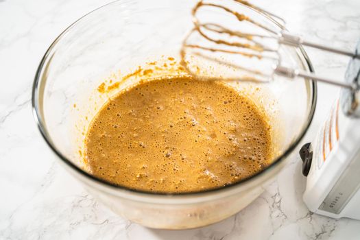 Mixing ingredients in a large glass mixing bowl to bake gingerbread cupcakes.