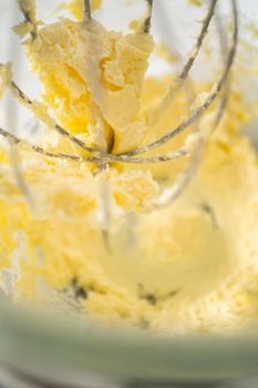 Mixing ingredients in a large glass mixing bowl of kitchen mixer to make eggnog buttercream frosting.