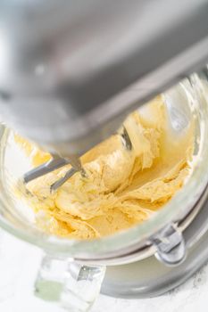 Whisking buttercream frosting in a glass mixing bowl with an electric kitchen mixer for American flag mini cupcakes.