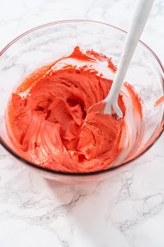 Mixing food coloring into the buttercream frosting to decorate American flag mini cupcakes.