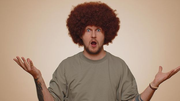 Excited amazed man 30s in t-shirt touching head and showing explosion, looking worried and shocked, professional burnout. Looking surprised wow guy isolated alone on beige studio wall background