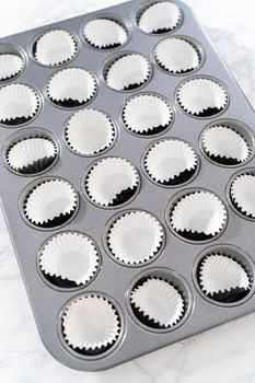 Scooping cupcake batter with dough scoop into a baking pan with liners to bake American flag mini cupcakes.