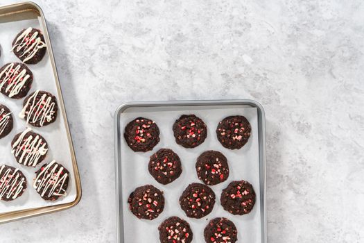 Flat lay. Drizzling melted white chocolate over freshly baked chocolate cookies with peppermint chips.